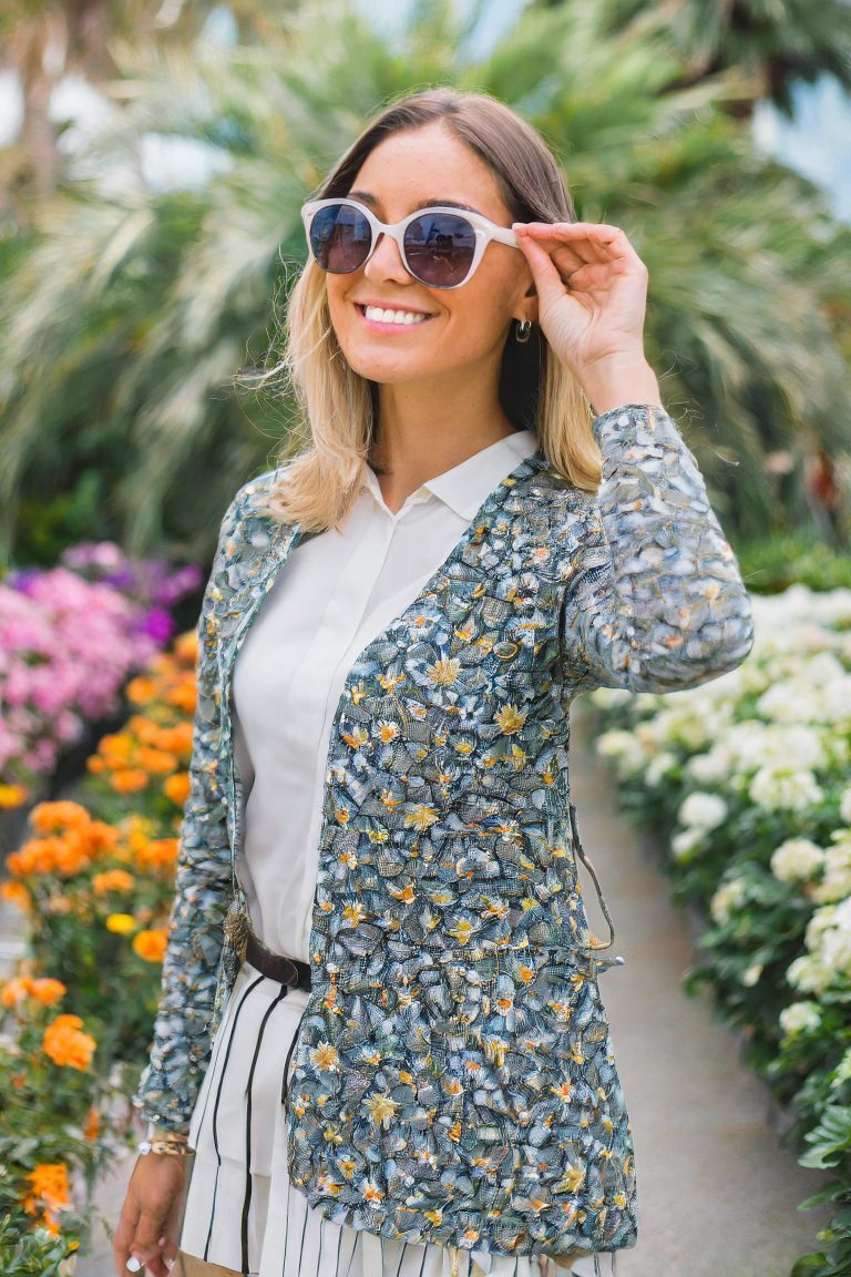 Firefly young woman dressed in trendy fashion with oval sunglasses, and blonde hair, outside a flowe